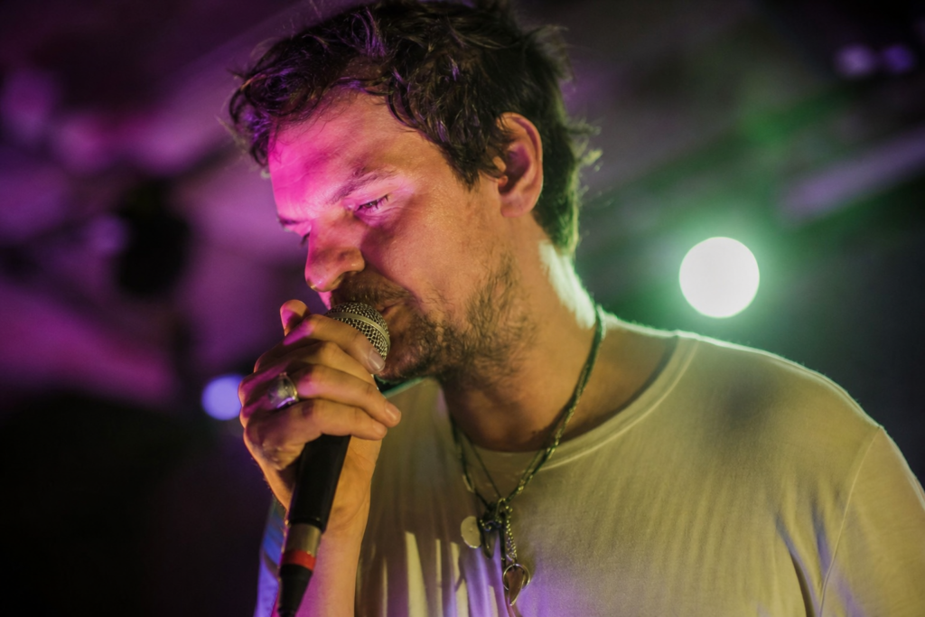 Tudor Chirila singing into a microphone on stage under green and purple lighting